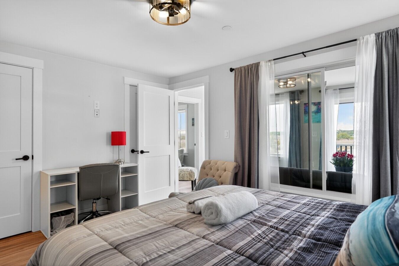A bedroom with a bed, a desk, a chair, and a window with curtains.