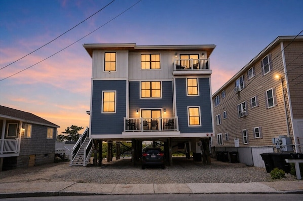 A two-story residential building with a balcony on the second floor, a covered entryway, and a car parked in front.