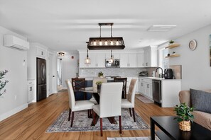 Una cocina moderna con gabinetes blancos, electrodomésticos de acero inoxidable y un comedor con una mesa redonda y sillas.
