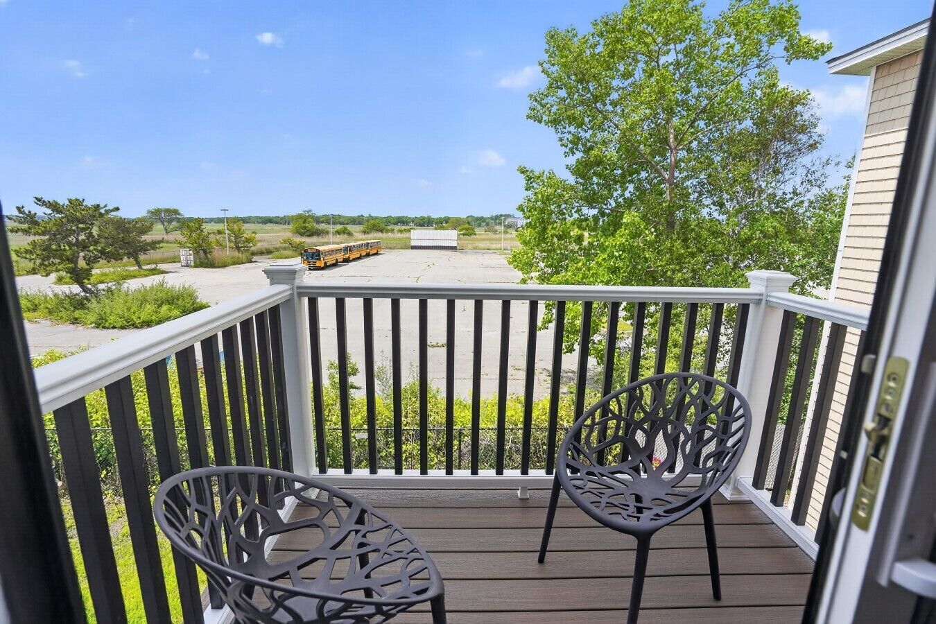 A balcony with two chairs, a view of a road, and a tree.