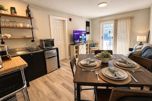 A modern kitchen with a built-in oven, a refrigerator, and a dining area with a wooden table set for four. - Steps to Beach, Ground Floor, Free Parking, King (Hampton)