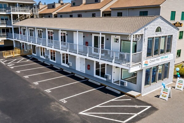A two-story motel with a balcony, a 'For Sale' sign, and a parking lot.
