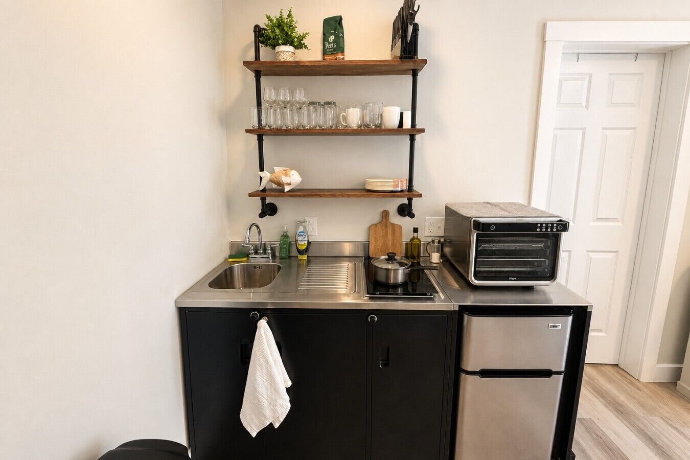 A compact kitchen with a sink, stove, toaster, and shelves above.