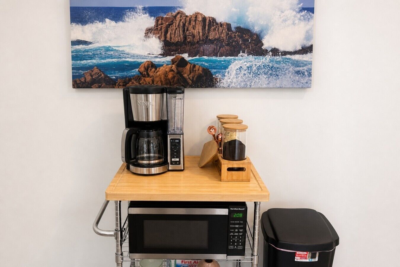 A kitchen area with a coffee maker, blender, microwave, and trash bin.