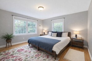 A bedroom with a bed, two bedside tables, a nightstand, a potted plant, and a window. - Sleep up to 12, quick access to Kittery and Portsmouth, Beaches, Boat Launch (Eliot)