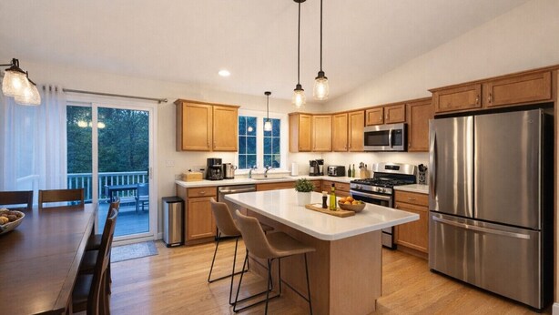 A modern kitchen with wooden cabinets, stainless steel appliances, and a large island with bar stools. - Sleep up to 12, quick access to Kittery and Portsmouth, Beaches, Boat Launch (Eliot)