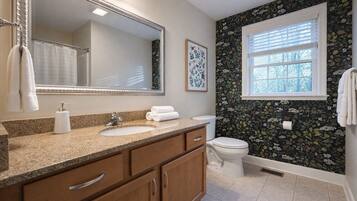 A bathroom with a granite countertop, a white sink, a toilet, and a window with blinds.