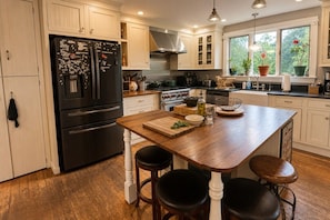 A kitchen with a central island, stainless steel appliances, and a window with plants.