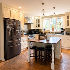 A kitchen with a central island, wooden stools, a stainless steel refrigerator, and a stove. - Great for group events, pool parties, and chefs looking to cook for large groups. (Eliot)