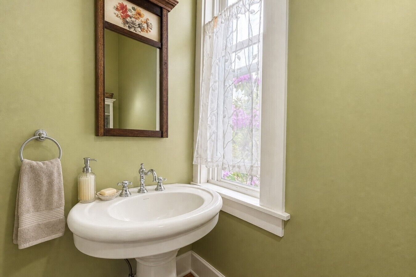 A bathroom with a white sink, a mirror, a towel rack, and a window with a view of flowers.