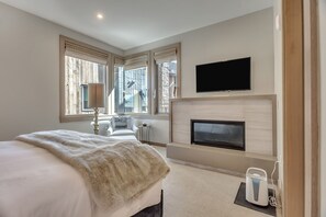 Ein modernes Hotelzimmer mit einem großen Bett, einem flachbildfernseher über einem Kamin und einem Fenster mit Blick nach außen.