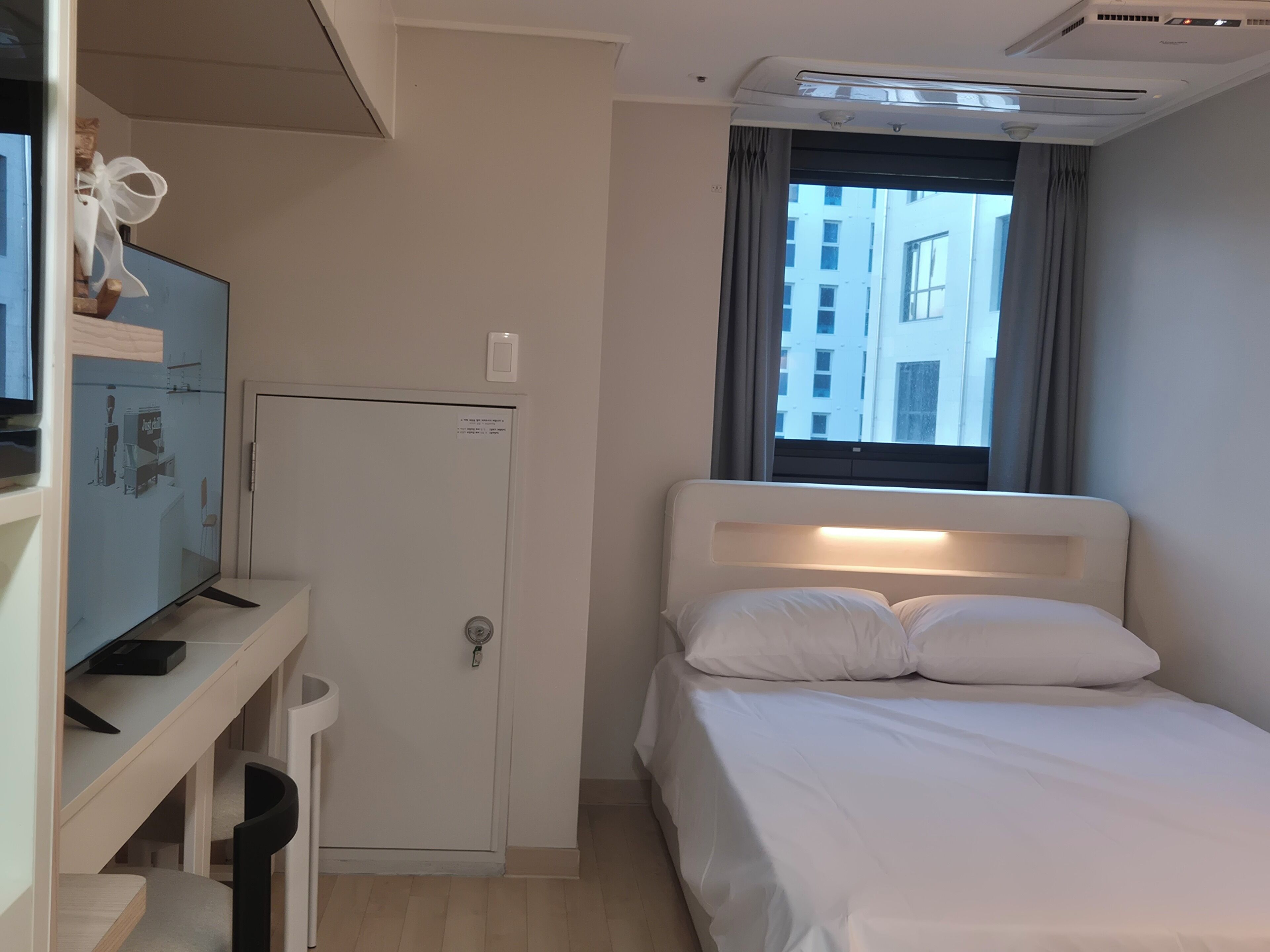 Habitación de hotel con cama, escritorio con computadora, televisión y ventana con cortinas.