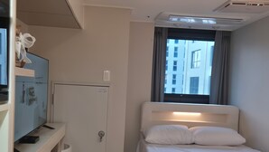 Ein Hotelzimmer mit Bett, Schreibtisch mit Computer, Fernseher und einem Fenster mit Vorhängen.
