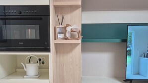 Eine Küche mit einem schwarzen Backofen, einem weißen Wasserkocher und einem hölzernen Regal mit Teekanne und einer kleinen Pflanze.
