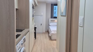 Ein enger Korridor führt zu einem Schlafzimmer mit einem Bett, einer kleinen Küchenzeile mit einer Waschmaschine und einer Tür mit einem Handtuchhalter.