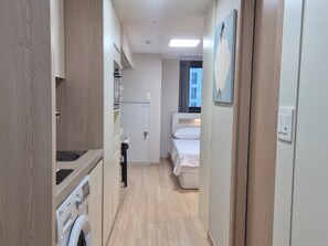 A narrow corridor leading to a bedroom with a bed, a small kitchenette with a washing machine, and a door with a towel rack. - 710ㅣDouble Bed Stay, Just 5 Minutes from Myeongdong Station (Seoul)