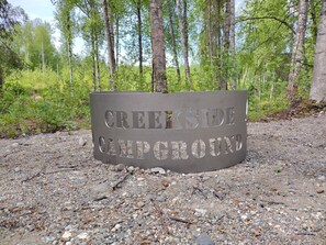 A metal sign with the text 'CREEKSIDE CAMPING GROUNDS' on a gravel surface.