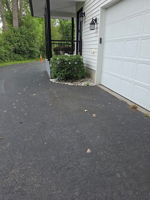 A driveway leading to a garage with a white garage door, a black railing, and a small bush with white flowers.