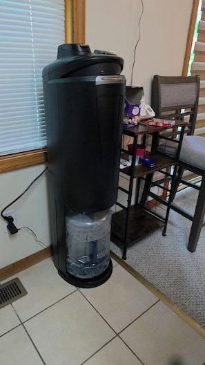 A water dispenser, a chair, and a table with a laptop and a game box.