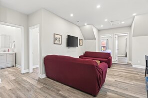 A spacious living area with a red sofa, a flat-screen TV mounted on the wall, and a wooden floor.