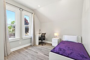 Ein Schlafzimmer mit Bett, Schreibtisch, Stuhl und einem Fenster mit Vorhängen.