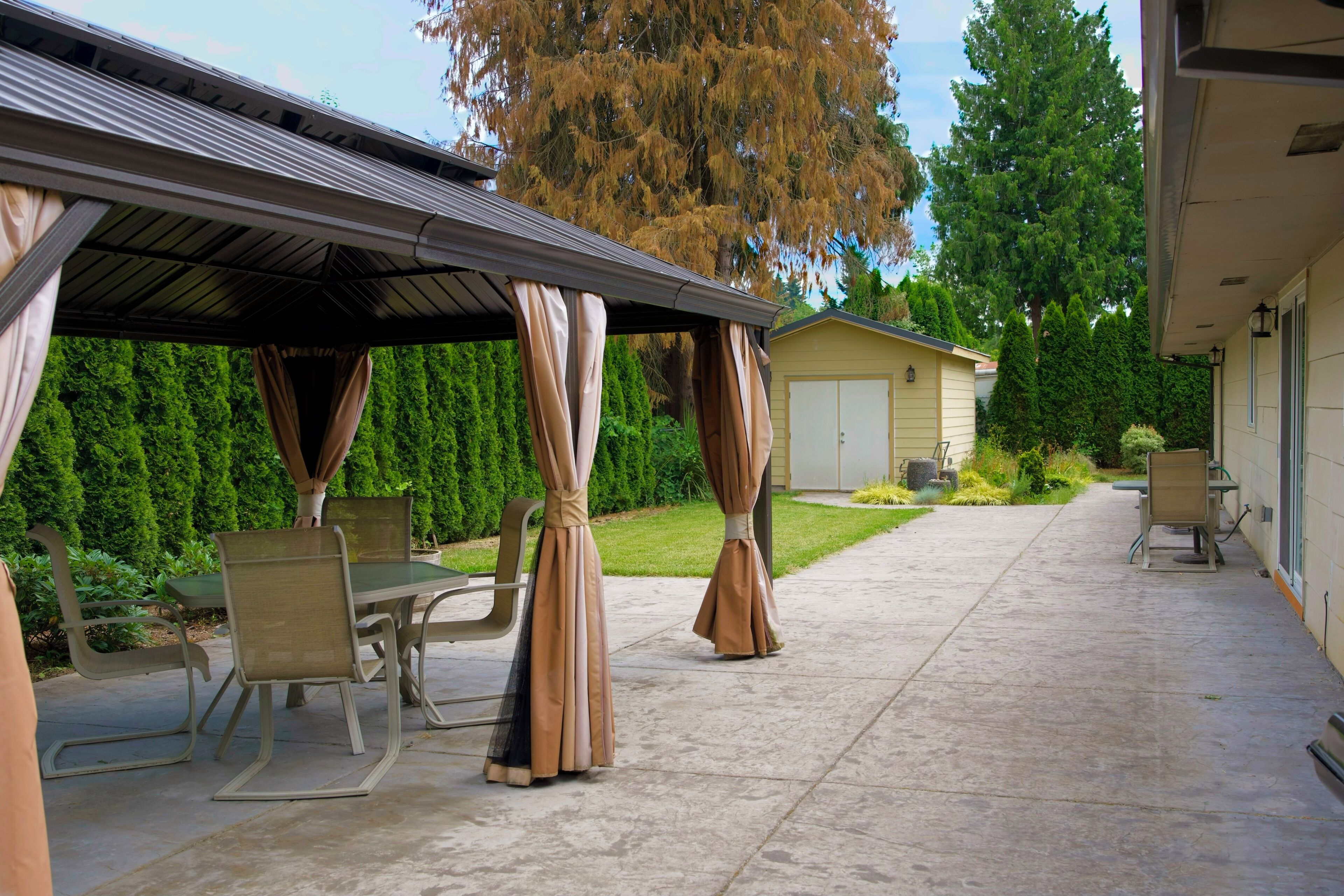 A covered patio area with a table and chairs, a garage, and a lawn.