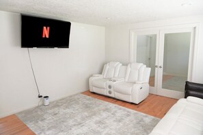 Ein modernes Zimmer mit einem wandmontierten Flachbildfernseher, einem weißen Sofa, einem grauen Teppich und einer Schiebeglastür.