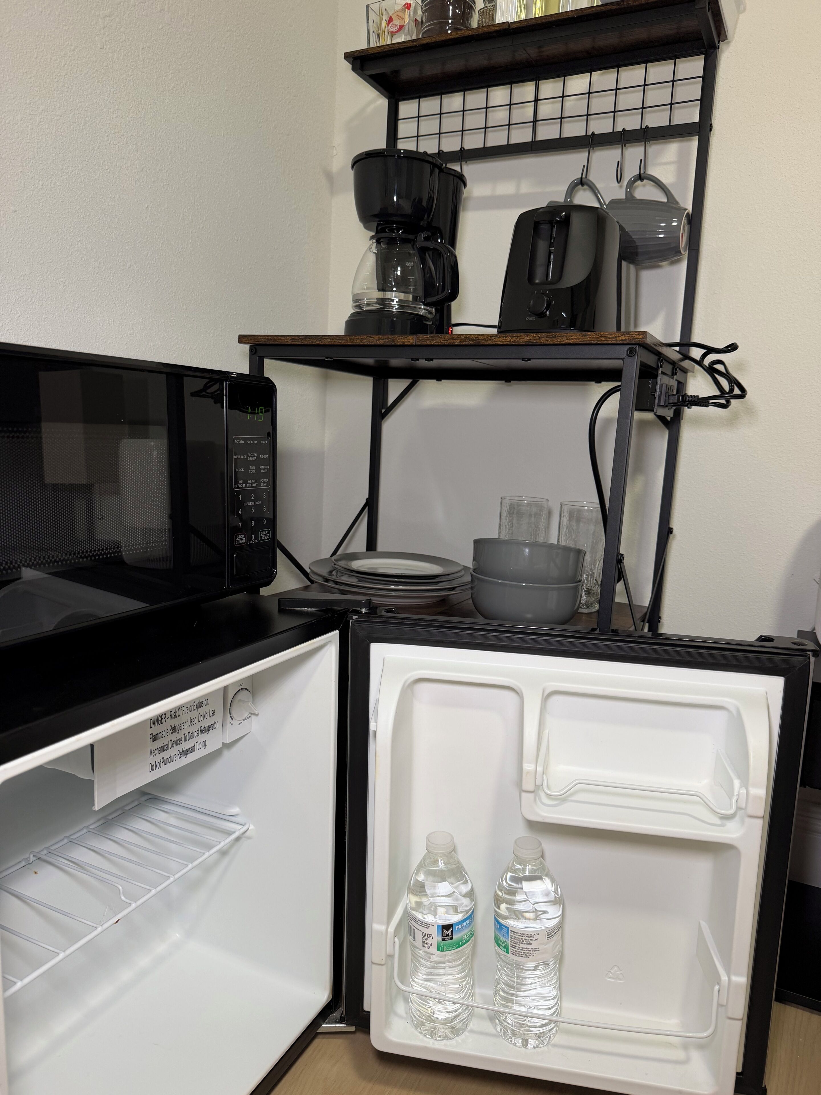 A compact kitchen with a microwave, a coffee maker, and a small refrigerator with two water bottles inside.