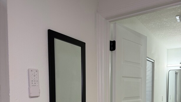 A hallway with a door, a mirror, and a bathroom with a sink and cabinets.