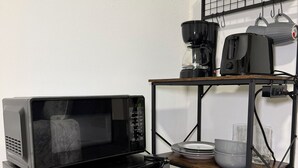 A compact kitchen with a microwave, a stainless steel mini-fridge, a coffee maker, and a shelf with kitchenware.