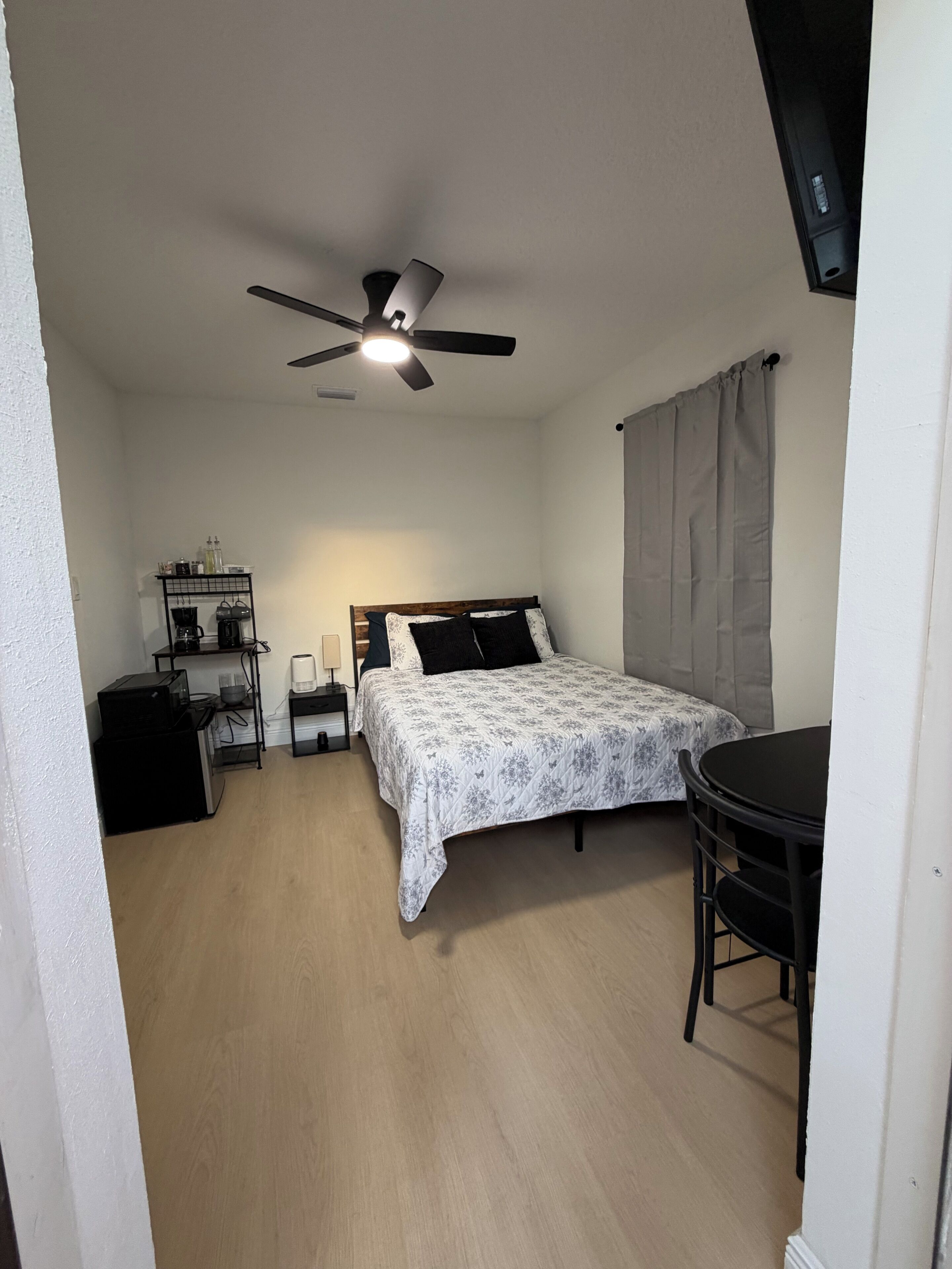 Una camera da letto con un letto, una scrivania, una sedia, una ventola a soffitto e una finestra con tende.