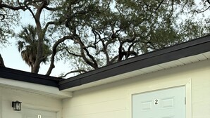 A building with two numbered doors, a green mat at the entrance, and a tree in the background.