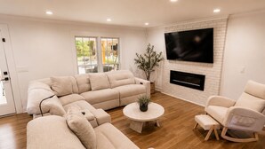 Una sala de estar moderna con un sofá modular, una mesa de centro redonda, una chimenea y un televisor de pantalla plana montado en una pared de ladrillo.