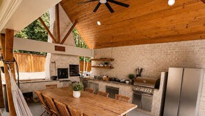 Una cocina con una mesa de madera, sillas, una parrilla y un refrigerador.