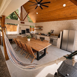 Una cocina con una mesa de madera, sillas, una parrilla y un refrigerador.
