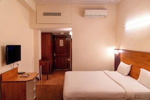 Habitación de hotel con cama, escritorio con televisor, silla de madera y puerta que da a otra habitación.