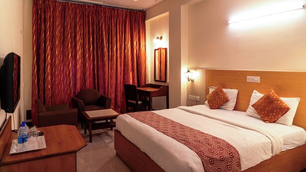 Ein Hotelzimmer mit Bett, Schreibtisch, Stuhl, Fernseher und Deckenventilator.