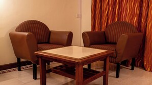 Ein Zimmer mit zwei Ledersesseln, einem Holztisch und einem gemusterten Vorhang.