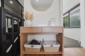 Ein modernes Interieur mit einem Holzkonsolentisch, Korbwäschekörben, einer Vase mit Trockenpflanzen und einem Spiegel.