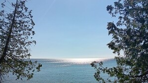 A beach with a clear sky, calm water, and a rocky shoreline. - Secluded Lake Michigan Retreat 4BR/4BA, EV Charging, Near Cave Point (Sturgeon Bay)