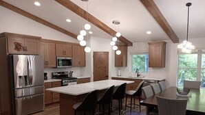 A modern kitchen with wooden cabinets, stainless steel appliances, and a central island with bar stools. - Secluded Lake Michigan Retreat 4BR/4BA, EV Charging, Near Cave Point (Sturgeon Bay)