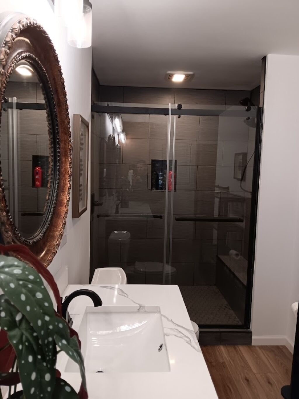 Une salle de bain moderne avec une porte de douche en verre, un lavabo blanc et un grand miroir.