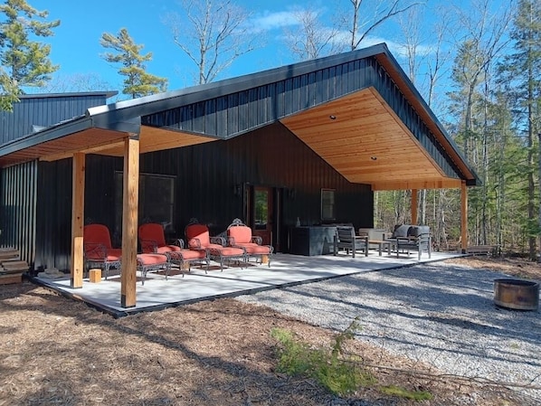 A modern cabin with a covered patio, outdoor seating, and a fire pit.