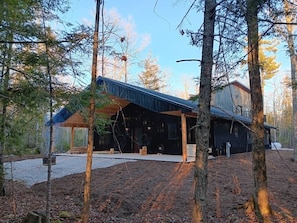 A modern cabin with a covered porch, surrounded by trees.