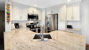 Una cocina moderna con armarios blancos, electrodomésticos de acero inoxidable, encimera de mármol y un lavamanos integrado.