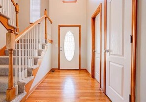 Un pasillo con una escalera de madera, una puerta con un tragaluz esmerilado y una puerta blanca a la derecha.