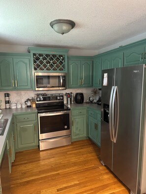 Una cocina con armarios color turquesa, un refrigerador de acero inoxidable, un microondas, una estufa y una vinoteca.
