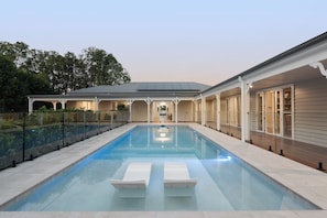 Ein Schwimmbecken mit Liegestühlen, einer überdachten Terrasse und Blick auf das Haus.