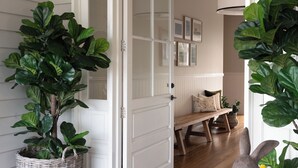 A hallway with a wooden bench, a wicker plant, and a door leading to another room. - Luxury Living In The Hinterland with a pool - 2 mins From
Town. (Maleny)