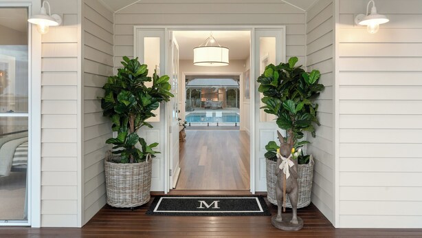 A house entrance with a wooden floor, a pool in the background, and two potted plants on either side.